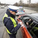 Policjant spisuje mandat, art. 97 kw. Kierowca w kamizelce odblaskowej zatrzymany do kontroli drogowej.