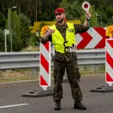 Strażnicy pilnują granica państwowa. Jeden z nich, w czerwonej beretce, kieruje ruchem, trzymając znak stop.