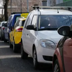 Rząd samochodów, w tym żółty Bolt Taxi, zaparkowany na chodniku.