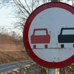 Znak drogowy zakaz wyprzedzania. Czerwony samochód z przodu, czarny z tyłu.