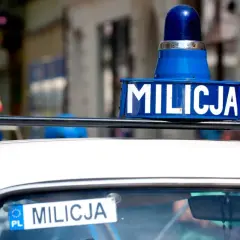 Niebieska lampa i napis "MILICJA" na dachu białego samochodu.