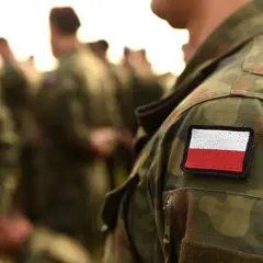 Żołnierz w mundurze polowym z naszywką flagi Polski. Weteran dumny ze swojej służby.