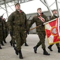 Żołnierze w mundurach maszerują z flagą. Uroczysta przysięga wojskowa w pełnym rynsztunku.