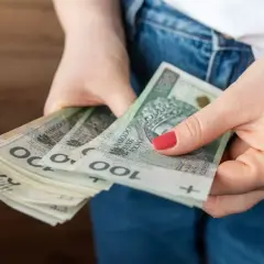 Dłonie trzymające stos banknotów 100 zł. Czy to przyszła kwota bazowa służba cywilna 2026?