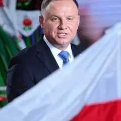 Prezydent Andrzej Duda z polską flagą, w tle ludowy strój. Może to symbolizować ułaskawienie i dumę narodową.