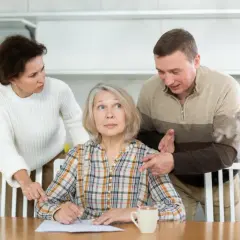 Zaniepokojona kobieta siedzi przy stole, podczas gdy jej syn i córka naciskają na nią.