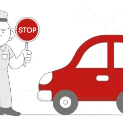 Znak STOP trzyma kierujący, zatrzymując czerwony samochód.