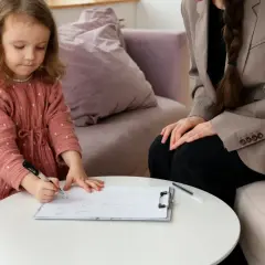 Mała dziewczynka rysuje, a obok siedzi kurator.