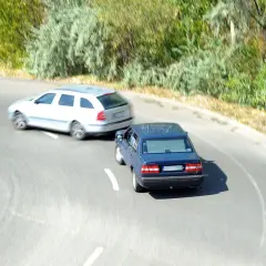 Niebezpieczne wymuszenie pierwszeństwa na zakręcie. Niebieski sedan wyprzedza białe kombi, ignorując zasady ruchu drogowego.