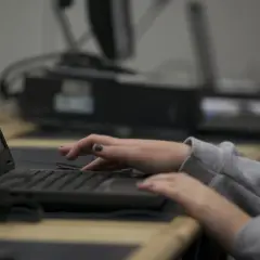Dłonie piszą na klawiaturze laptopa, jakby śledziły coś w internecie.