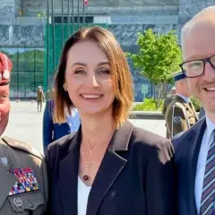 Dowódca generalny rodzajów sił zbrojnych w towarzystwie kobiety i mężczyzny w garniturze, na tle nowoczesnego budynku.