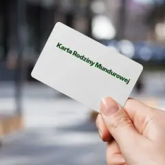 Dłoń trzyma białą kartę z napisem "Karta Rodziny Mundurowej" w kolorze zielonym.