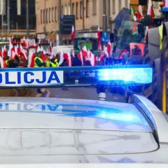 Policyjny radiowóz z włączonym sygnałem świetlnym na tle protestu rolników z flagami. Czy to jego jaka odprawa po 20 latach w policji?
