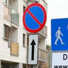 Znak zakaz postoju informuje, że nie można tu parkować. Obok znak drogi wewnętrznej z ikonami pieszych i samochodu.