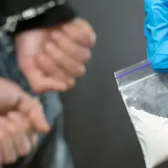 Ręce w kajdankach, obok woreczek z białym proszkiem, prawdopodobnie klefedron.