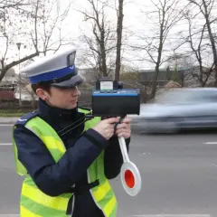 Policjantka w kamizelce odblaskowej mierzy prędkość przejeżdżającego samochodu radarem.