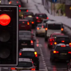Czerwone światło sygnalizatora drogowe, a za nim sznur samochodów stojących w korku. Niektórzy kierowcy ignorują zakaz, ryzykując przejazd na czerwonym świetle.