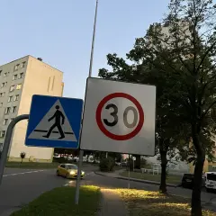 Znak D43 (przejście dla pieszych) i znak ograniczenia prędkości do 30 km/h na tle bloków mieszkalnych i drzew.