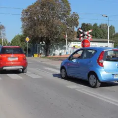 Czerwony i niebieski samochód na przejściu dla pieszych, czerwony czeka na wymijanie, niebieski już rusza.