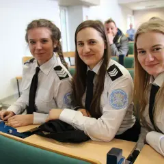 Trzy uśmiechnięte studentki w mundurach policyjnych siedzą w sali wykładowej. To przyszłość policji, ich studia policyjne dopiero się zaczynają.