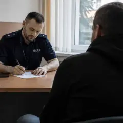 Policjant spisuje zeznania podejrzanego w pokoju przesłuchań.