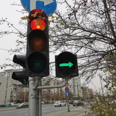 Sygnalizator S2 z czerwonym światłem na górze i zieloną strzałką w prawo. Za nim drzewa i budynki.