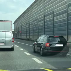 Kork na autostradzie, samochody i ciężarówki stoją w korku. Widać znak informujący o jeździe na suwak.