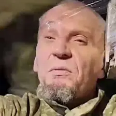 Łysy mężczyzna z brodą, ubrany w mundur, wygląda na zmęczonego. To jeniec wojenny.