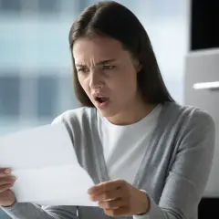 Zaskoczona kobieta czyta dokument, który może dotyczyć jej stosunku pracy.