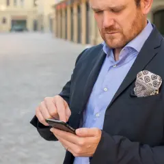 Mężczyzna w garniturze sprawdza telefon, być może logując się za pomocą danych biometrycznych.