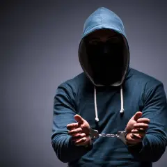 Mężczyzna w kapturze i masce na twarzy, z rękami w kajdankach, symbolizujący zatarcie skazania i szansę na nowy początek.
