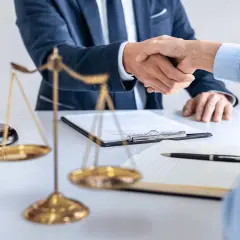 Uścisk dłoni prawników przy biurku z wagą sprawiedliwości i młotkiem. Sprawa 157 kk zakończona sukcesem.