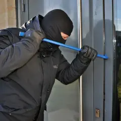 Złodziej w kominiarce i rękawiczkach próbuje wyważyć drzwi łomem. To może być próba włamania, zgodnie z art. 279 kk.
