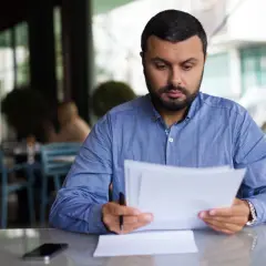 Mężczyzna w niebieskiej koszuli analizuje dokumenty, być może dotyczące umorzenia długu lub projektu.