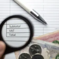 Pod lupą widać napisy "Subtotal", "VAT", "Total" na tle dokumentu z cyframi. Obok leżą banknoty i monety, co sugeruje analizę finansową zgodną z art. 96 ust. 9a pkt 2.