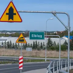 Znak drogowy "ustąp pierwszeństwa" i przejazd kolejowy ostrzegają przed niebezpieczeństwem na drodze podporządkowanej do Elbląga.
