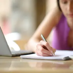 Kobieta pisze ręcznie, obok laptop i kawa. Może to być umowa na czas określony.