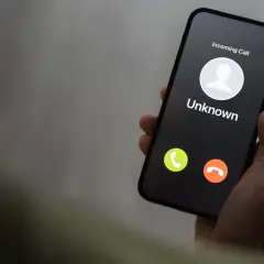 Dłoń trzyma smartfon z ekranem blokady, na którym widnieje "Incoming Call" od nieznanego numeru. Uważaj na vishing!