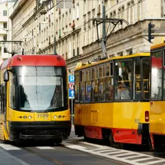 Dwa żółto-czerwone tramwaje stoją na ulicy, jeden z nich ma pierwszeństwo.