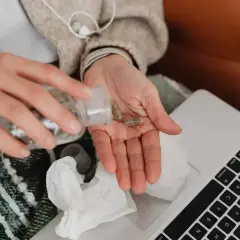 Dłonie z kapsułkami leków, obok laptop i chusteczki. Kto płaci za L4, gdy choroba dopada w domu?