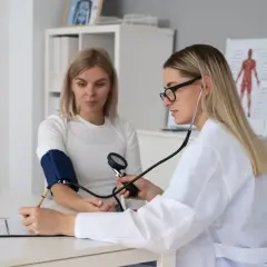 Lekarka w białym kitlu bada ciśnienie pacjentce. To może być część badań do komisji lekarskiej w policji.
