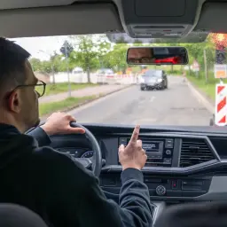 Kierowca w okularach wskazuje palcem na ekran nawigacji, gdy zbliża się do drogi dla pieszych.
