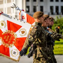 Żołnierze niosą biało-czerwony proporzec z godłem i dewizą "Bóg, Honor, Ojczyzna".