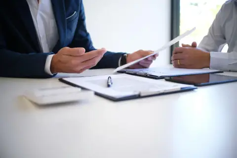 Dwóch mężczyzn omawia dokumenty, być może związane z art. 55 Kodeksu pracy. Na stole leżą dokumenty, tablet i kalkulator.