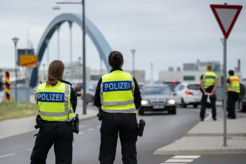 Policjanci w kamizelkach z napisem POLIZEI prowadzą kontrole na granicy niemieckiej. Ruch samochodowy jest spowolniony.