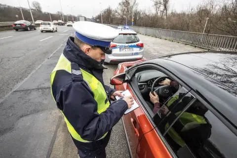 Policjant spisuje mandat, art. 97 kw. Kierowca w kamizelce odblaskowej zatrzymany do kontroli drogowej.