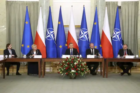 Spotkanie przy stole z flagami Polski, UE i NATO. Dyskusja o bezpieczeństwie i artykuł 5 NATO.
