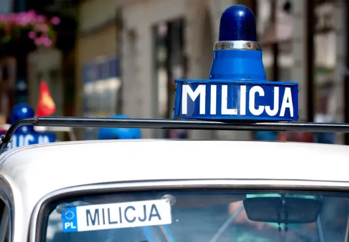 Niebieska lampa i napis "MILICJA" na dachu białego samochodu.