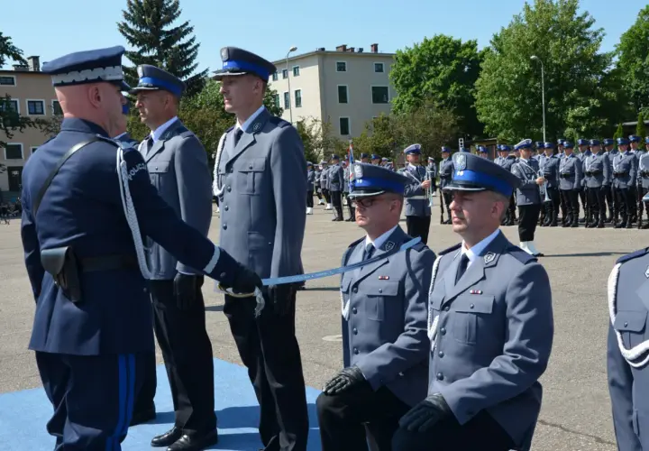 Uroczyste mianowanie na nowych zasadach. Policjanci w galowych mundurach, jeden klęczy, otrzymując szablę.