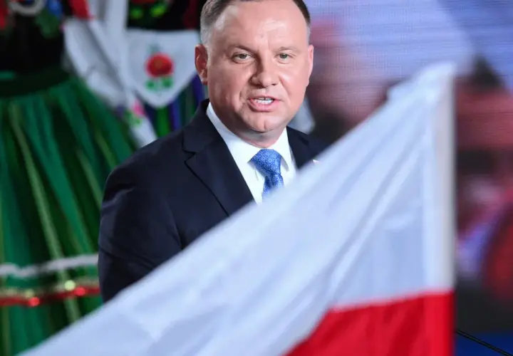 Prezydent Andrzej Duda z polską flagą, w tle ludowy strój. Może to symbolizować ułaskawienie i dumę narodową.
